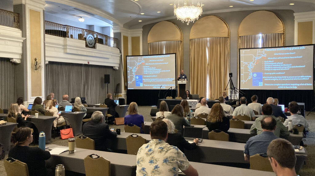 Attendees at the Forum watch a speaker standing in front of large screens give a presentation 